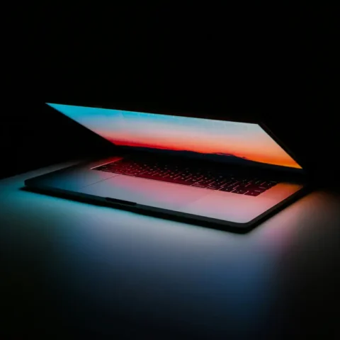 Portátil abierto en la oscuridad con la pantalla iluminada en tonos azul y naranja de atardecer