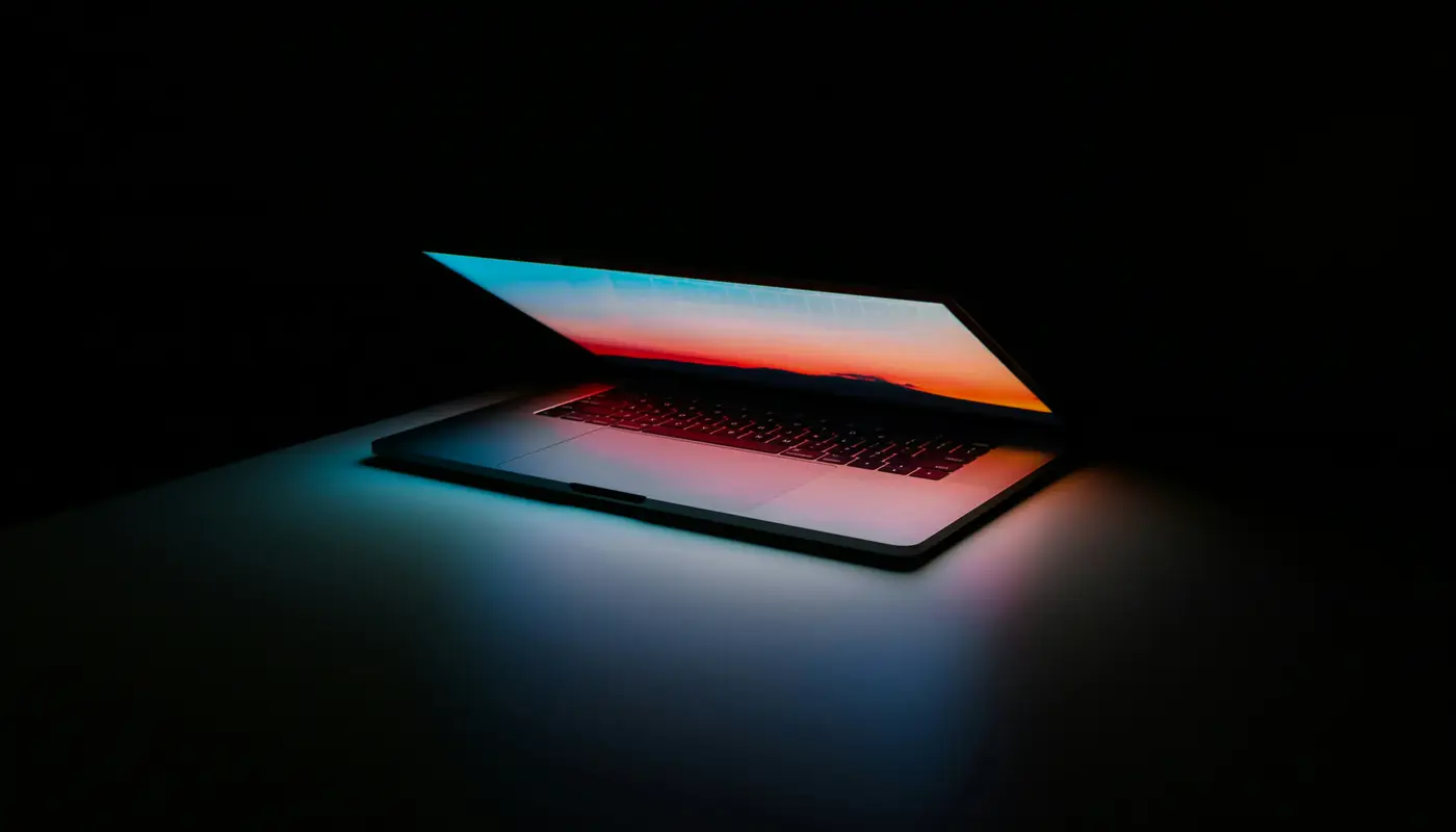 Portátil abierto en la oscuridad con la pantalla iluminada en tonos azul y naranja de atardecer