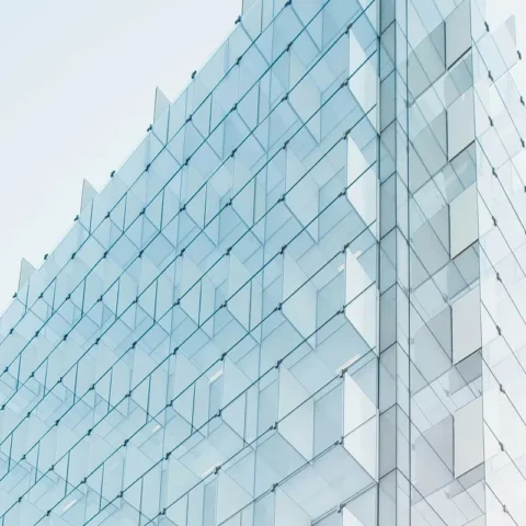 Fachada de un edificio de cristal moderno fotografiada en ángulo ascendente, con reflejos azulados